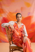 Woman in an orange outfit sitting on a wooden chair against a colorful abstract background